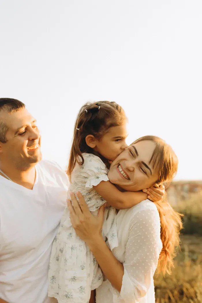 A father, mother, and daughter laughing together outdoors at golden hour